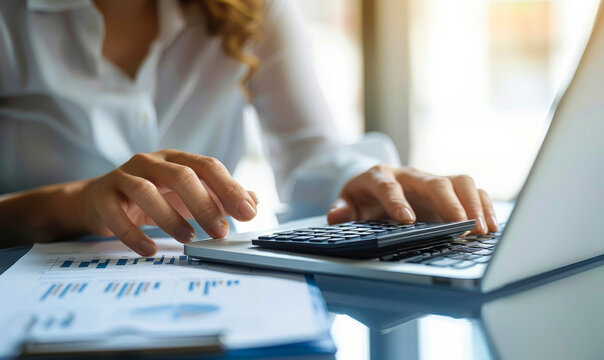 Middle-aged businesswoman in formal wear calculating taxes, accounting with laptop, calculator on office desk - finance, tax season concept