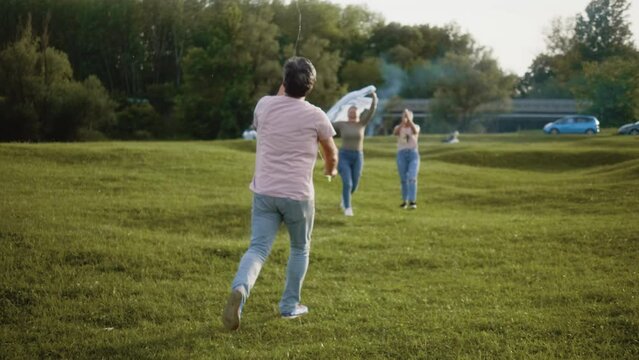 Medium shot of a senior grandparents with adult daughter playing together flying a kite toy on a green meadow in nature