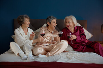 Beautiful female senior friends in pajamas drinking wine enjoying fun retirement