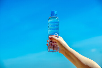A girl holds a bottle of drinking water in her hand against a blue sky background
