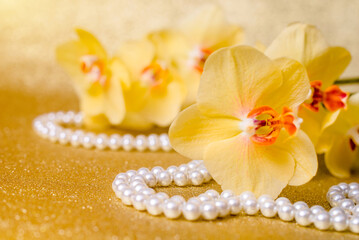 yellow Orchid and pearl necklace on a shiny gold background
