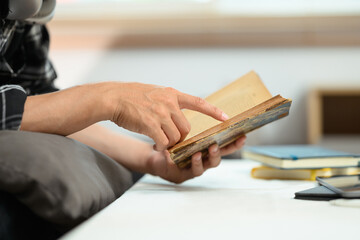 Fototapeta premium Young man relaxing on couch and reading book, enjoying free time on weekend at home