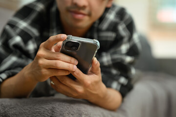 Cropped shot adult asian man lying on couch and using mobile phone