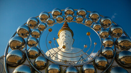 Large, white Buddha statue with a serene expression, surrounded by a circular structure adorned with multiple reflective spheres. The statue is depicted in a traditional style, complete with intricate