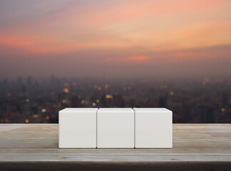 Three white block cubes on wooden table over blur of cityscape on warm light sundown