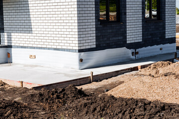 Detailed closeup of the foundation and wall of a newly constructed modern brick house with black and white tiles, showcasing the solid base and modern design of the building