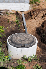 Manhole cover next to pipe in dirt, surrounded by grass and soil