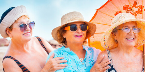 Group mature women wearing beach hats and smiling while standing on a tropical beach. Older ladies...