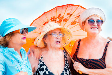 Group mature women wearing beach hats and smiling while standing on a tropical beach. Older ladies...