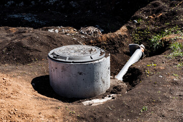 Concrete septic tank sits in dirt by pipe, surrounded by grass and rocks