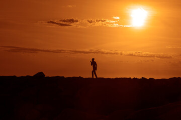 Fototapeta premium Work and leisure. black silhouette of busy business man walking, talking at mobile cell phone on horizon line opposite sunset cloudy sky. Summer season. step by step to success. human figure.