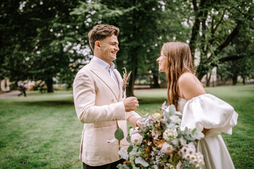 Riga, Latvia, - August 26, 2024 - Bride and groom laughing together in a park, groom holding...