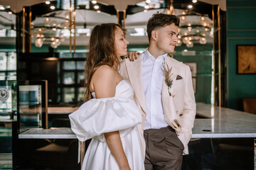 Riga, Latvia, - August 26, 2024 - A couple dressed in wedding attire looks at each other, standing at a bar with elegant lighting.