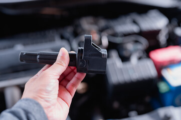 The automotive technician inspects the ignition coil during car maintenance, ensuring the engine's...