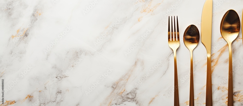Aufkleber design concept with clean golden metal cutlery on a light marble background in a top view copy space