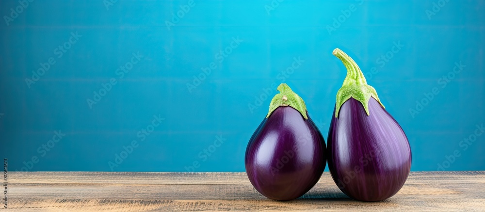 Poster a copy space image featuring two eggplants elegantly placed on a wooden table with a beautiful blue 