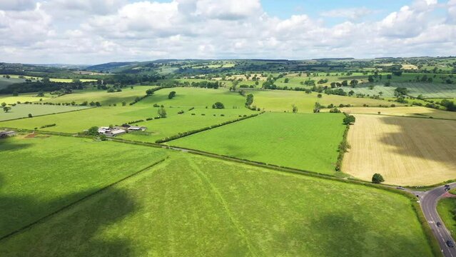 Aerial drone footage of the beautiful village and civil parish of Pool in Wharfedale in West Yorkshire England showing the farmers fields and traffic on the road on a sunny day in the summer time