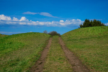 Fototapeta na wymiar Walkway path rural trail or road in green fields between two hills. Summer day in countryside. 