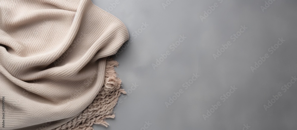 Poster copy space image of a beige knitted blanket resting elegantly on a gray concrete background evoking 