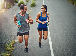 Fitness, running and couple with smile, race and bottle for hydration with water and outdoor. Road,...