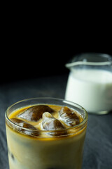 Iced coffee in glass near milk pitcher on grey background 