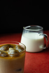 Iced coffee near milk pitcheron red back black background