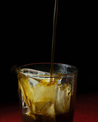 Black coffee pouring in glass with ice on black and red background 
