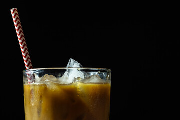 Coffee with ice and milk in glass with drinking straw isolated on black 