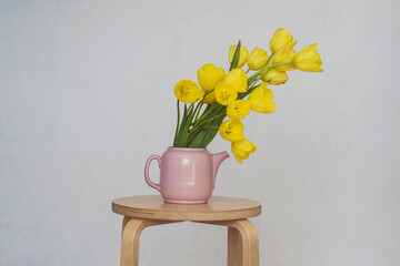 Spring flowers. Yellow tulips. Tulips in a pink teapot. Minimalist interior. Vintage look. Scene with yellow flowers. Combination of pink and yellow.