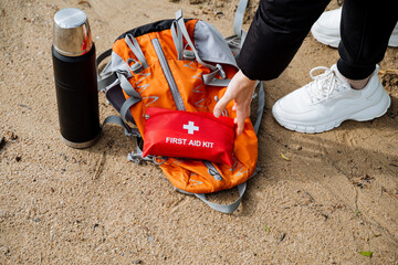 Hiker with red backpack, first aid kit, and thermos prepares for outdoor adventure in nature. Ready...