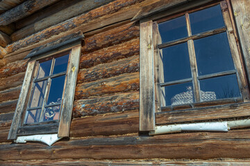 A wooden house made of logs. The windows of an old village house built in the 19th century. Cracked dark logs of a wooden house.