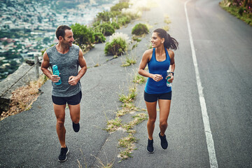 Fitness, running and couple with smile, routine and bottle for hydration with water and outdoor. Road, exercise and people in morning, sportswear and training together, energy and workout for race