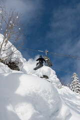 A snowboarder in a black suit jumps from a snow inflatable under a chairlift in the forest at the Rusutsu resort in Hokkaido