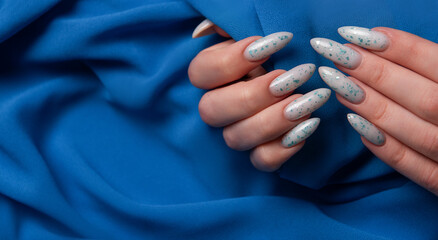 Female hands with blue nail design on blue textile background.