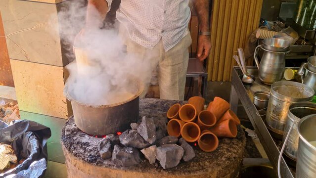 Close up indian man making a pot of tandoori tea over hot coals with clay earthenware cups heating on the side to serve in Jaipur, Delhi, Lucknow