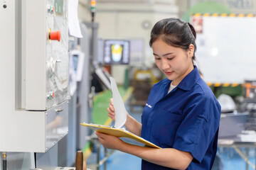 Asian woman industrial engineer wearing uniform checking of work list on clipboard with automated...