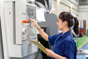 Asian woman industrial engineer wearing uniform hold a clipboard checking of automated machinery in...