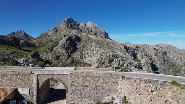 A cyclist rides on a stone bridge in the mountains