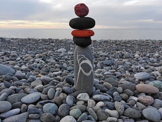 Stones pyramid or tower on pebble beach symbolizing stability, zen, harmony, balance. Pebble tower or pyramid pile on the seaside. Pyramidal tower of pebbles on the coast. Stack of different pebbles.