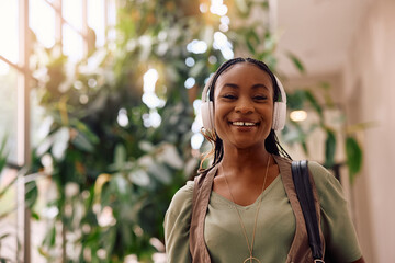 Happy creative black woman wearing headphones while working in office and looking at camera.