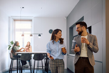 Happy entrepreneurs talking while drinking coffee in office kitchen.