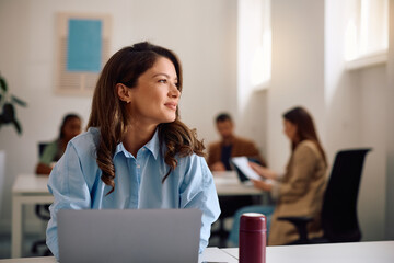 Happy businesswoman working on laptop at start up office and looking away.