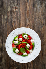 Caprese salad - tomatoes and mozzarella balls served in white bowl on wooden background
