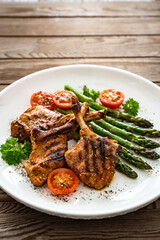 Lamb chops with bone and cooked green asparagus on wooden table
