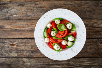 Caprese salad - tomatoes and mozzarella balls served in white bowl on wooden background

