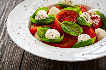 Caprese salad - tomatoes and mozzarella balls served in white bowl on wooden background
