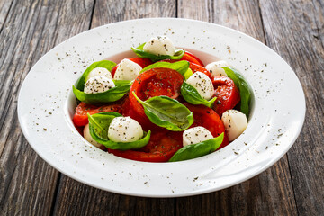 Caprese salad - tomatoes and mozzarella balls served in white bowl on wooden background
