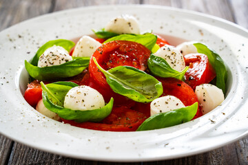 Caprese salad - tomatoes and mozzarella balls served in white bowl on wooden background

