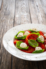Caprese salad - tomatoes and mozzarella balls served in white bowl on wooden background

