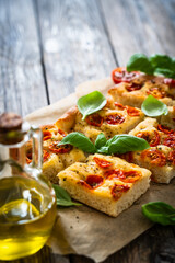 Focaccia - baked sandwich with tomatoes and basil leaves on wooden table